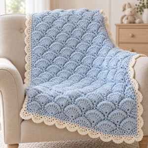 May include: A light blue crochet blanket featuring a repeating fan or scallop stitch pattern throughout the center. The blanket is finished with a decorative cream-colored scalloped border that frames the entire rectangular textile piece.