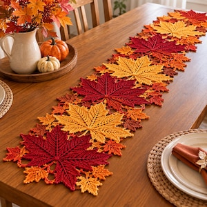 May include: A crochet table runner featuring a repeating pattern of maple leaves in shades of deep red, bright orange, and golden yellow. The runner is laid out on a wooden table, showcasing intricate yarn textures and leaf-shaped edges.