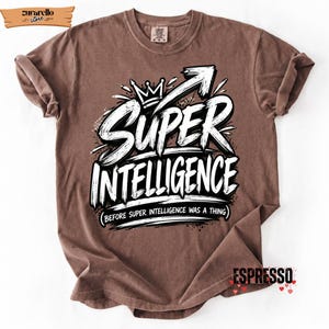Op de afbeelding: Een bruin t-shirt met korte mouwen en een witte grafische print met een kroonpictogram en de tekst "SUPER INTELLIGENCE" gevolgd door de kleinere tekst "(BEFORE SUPER INTELLIGENCE WAS A THING)" en het woord "ESPRESSO" rechtsonder.