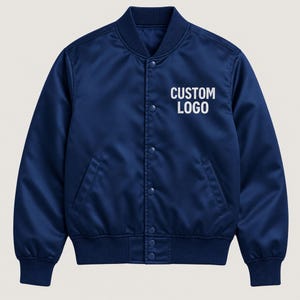 Può includere: Un giubbotto bomber blu navy con colletto, polsini e orlo a coste. La giacca presenta una chiusura frontale con bottoni a pressione e due tasche laterali. Il testo CUSTOM LOGO è stampato in bianco sulla parte superiore sinistra del petto.
