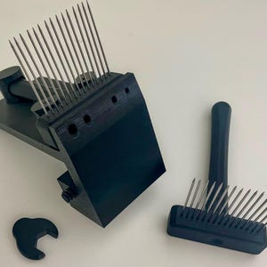 May include: A black fiber blending tool set featuring a main block with a row of long, thin metal needles, a separate handheld comb with metal tines, and a small, black, C-shaped adjustment component for fiber processing.