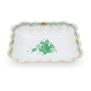 Op de afbeelding: Een rechthoekig dienblad van wit porselein met geschulpte randen, voorzien van een centraal groen bloemmotief en een decoratieve groene bladrand. De rand is afgewerkt met goudkleurige accenten en kleine gouden details op de hoeken en zijkanten.