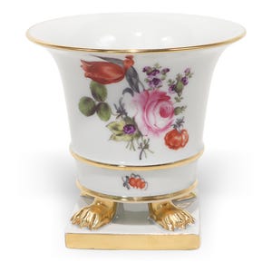 May include: A white porcelain vase featuring a hand-painted floral arrangement with pink, red, and purple blossoms. The vase has a flared rim with a gold-painted edge, gold bands around the body, and stands on four gold-painted lion paw feet.