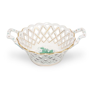 Könnte beinhalten: Eine weiße Porzellanschale mit gitterartigem Durchbruchmuster, verziert mit goldfarbenen Rändern und Griffen. Der Innenboden zeigt ein grünes Blumenmotiv. Die Schale hat zwei geschwungene Griffe und einen gewellten Rand, was die feine Verarbeitung unterstreicht.