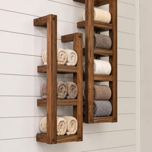 May include: Two wall-mounted wooden towel racks with a dark brown finish. The left rack has three shelves holding four rolled towels in beige and brown. The right rack has four shelves holding four rolled towels in beige, brown, and gray.
