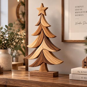 Puede incluir: Una escultura decorativa de árbol de Navidad de madera con ramas curvas superpuestas en tonos de madera claros y oscuros alternos, rematada con una estrella de cinco puntas y montada sobre una base rectangular de madera.