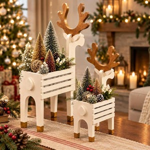 Peut inclure: Deux jardinières en bois blanc en forme de renne avec des bois de couleur bois naturel. Chaque jardinière est remplie de sapins miniatures en brosse, de petites pommes de pin, de baies blanches et de sphères décoratives dorées.