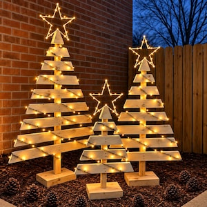 Puede incluir: Tres estructuras triangulares de árbol de Navidad hechas de listones de madera clara horizontales, cada una montada sobre una base cuadrada de madera. Cada árbol está envuelto en luces blancas cálidas y coronado con una estrella de alambre brillante.