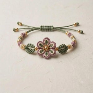 May include: A macrame bracelet featuring a central flower motif with mauve and sage green cord petals, a gold-toned center bead, and two sage green leaf-shaped accents. The band consists of alternating mauve, cream, and sage green knots with gold beads.