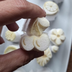 Puede incluir: Un objeto cilíndrico de espuma blanca porosa con una superficie texturizada y una sección transversal que revela un patrón curvo en forma de corazón de color amarillo pálido. El material parece suave y ligero, con una estructura celular visible.