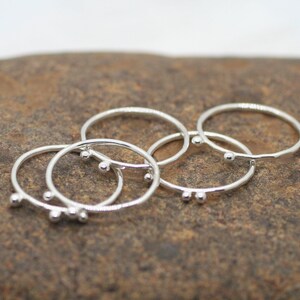 Puede incluir: Conjunto de cuatro anillos de plata con pequeñas cuentas. Los anillos están apilados uno encima del otro.