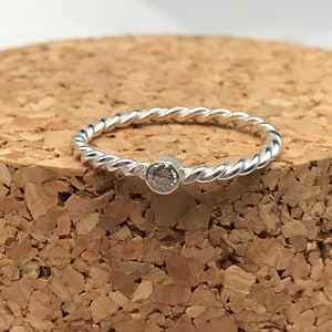 Puede incluir: Un anillo de plata con una banda trenzada y una pequeña piedra transparente en el centro.