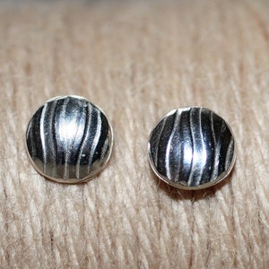 Puede incluir: Un par de pendientes de botón de plata con un diseño texturizado ondulado.