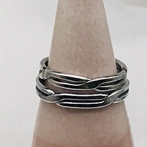 Puede incluir: Un anillo de plata con un diseño trenzado. El anillo está hecho de tres bandas que están entrelazadas.