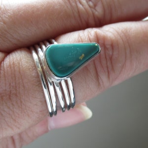 Puede incluir: Un anillo de plata con una piedra turquesa verde engastada en forma triangular. El anillo está apilado con otras cuatro bandas de plata.