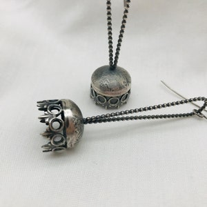 Puede incluir: Un par de pendientes de plata con forma de corona en la parte superior y una cadena que cuelga. Los pendientes están sobre un fondo blanco.