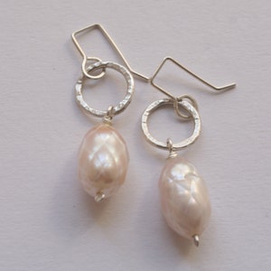 Puede incluir: Un par de pendientes de plata con un diseño de círculo martillado y una perla de agua dulce rosa.