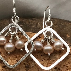Puede incluir: Pendientes de plata con un marco cuadrado y tres perlas rosadas colgando de la parte inferior.