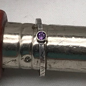 Puede incluir: Un anillo de plata con una banda texturizada y una pequeña piedra preciosa púrpura.