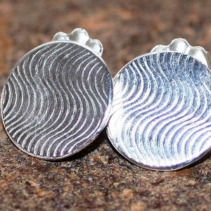 Puede incluir: Un par de pendientes de plata con un patrón ondulado. Los pendientes son redondos y tienen un acabado liso.