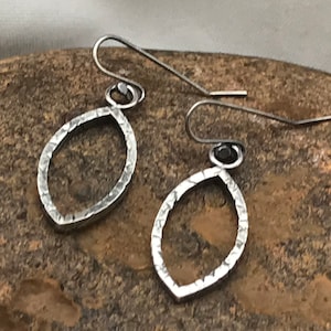 Puede incluir: Un par de pendientes de plata con un diseño ovalado martillado. Los pendientes tienen un cierre simple de gancho de alambre.