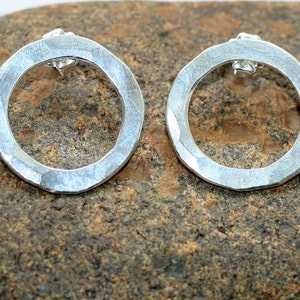 Puede incluir: Un par de pendientes de círculo martillados de plata. Los pendientes son simples y modernos, con una textura martillada que les da un aspecto único.