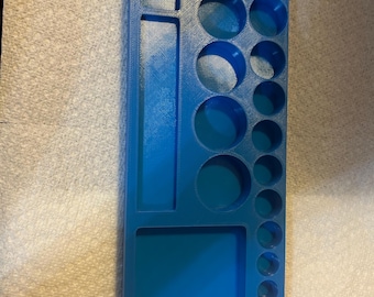 May include: A rectangular blue plastic organiser tray featuring a variety of recessed compartments. The layout includes two long rectangular slots, one large square section, and a series of circular holes of varying sizes arranged in columns.