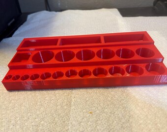 May include: A bright red plastic organiser tray featuring a tiered design. The top tier has three rectangular compartments, the middle tier contains seven circular holes, and the bottom tier features fifteen smaller circular holes for storage.