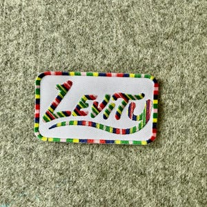 Peut inclure: Un &eacute;cusson rectangulaire brod&eacute; avec un fond blanc et une bordure ray&eacute;e multicolore. Le mot Levity est cousu au centre avec un motif de fil ray&eacute; multicolore assorti &agrave; la bordure, pr&eacute;sentant un style d'&eacute;criture cursive manuscrite.