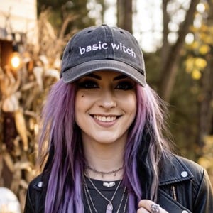 Könnte beinhalten: Eine anthrazitfarbene Baseballkappe mit dem in Weiß gestickten Text basic witch auf der Vorderseite. Die Kappe hat einen gebogenen Schirm und eine strukturierte Krone aus gewaschenem Stoff mit sichtbaren Nähten entlang der Kanten.