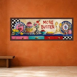 Pode incluir: Uma impressão de arte de parede retangular emoldurada apresentando uma cena de cozinha com tigelas empilhadas coloridas, um vaso de flores, um pedaço de manteiga e duas colheres antropomórficas. O texto MORE BUTTER está impresso em vermelho.