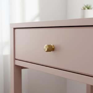 May include: A light pink wooden drawer unit featuring a single horizontal drawer with a cylindrical, textured brass-toned metal knob centred on the front panel. The furniture piece has a smooth, matte finish and a clean, rectangular frame design.