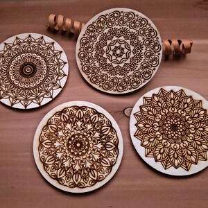May include: Four wooden coasters with intricate laser-cut mandala designs. Each coaster features a different pattern in shades of brown.