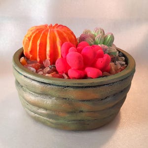 May include: A green ceramic planter with a textured surface holds a small succulent garden. The garden includes a bright orange cactus, a pink succulent, and a green succulent.