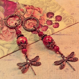 May include: A pair of dangle earrings with a red and white marbled stone bead, a bronze floral charm, and a bronze dragonfly charm.