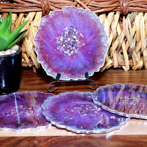 May include: Set of four purple and silver resin coasters with a glittery finish. The coasters have a unique agate design with embedded crystals.
