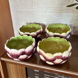 Może przedstawiać: Cztery ceramiczne miski w kształcie karczochów, każda z żywym limonkowym wnętrzem i zewnętrzem z nakładającymi się warstwami przypominającymi płatki w odcieniach głębokiego fioletu i kremu, ułożone w formacji dwa na dwa na płaskiej powierzchni.