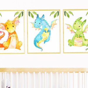 May include: Three framed watercolor paintings of cartoon dragons. The dragons are orange, blue, and green. Each dragon has a different expression and pose.