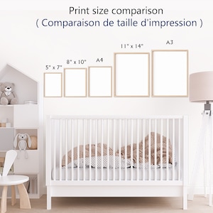 May include: A white crib with a brown and white patterned blanket. The crib is in a nursery with a white bookshelf, a white bunny chair, and a lamp with a pink shade. The wall has a print size comparison chart with different sizes of prints in inches and centimeters.