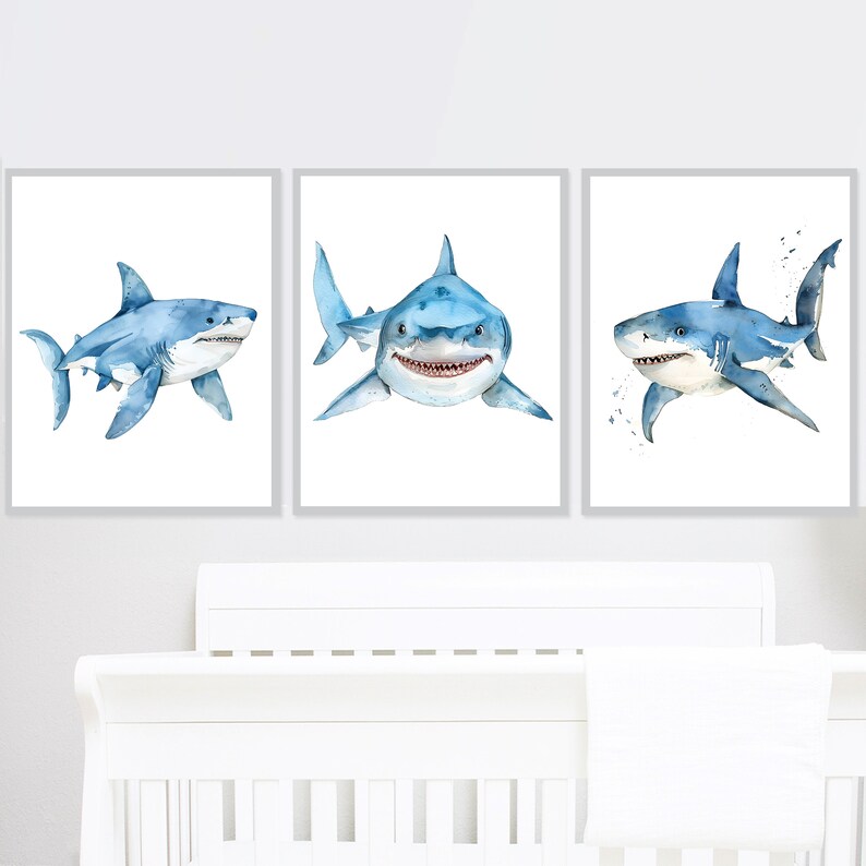 May include: Set of three watercolor paintings featuring blue sharks on a white background. The sharks are depicted in different poses, with one swimming towards the viewer, one swimming away, and one swimming sideways.