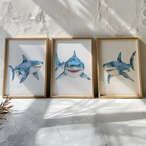 May include: Three framed watercolor paintings of blue and white sharks. Each painting features a different shark pose, with one shark looking directly at the viewer.