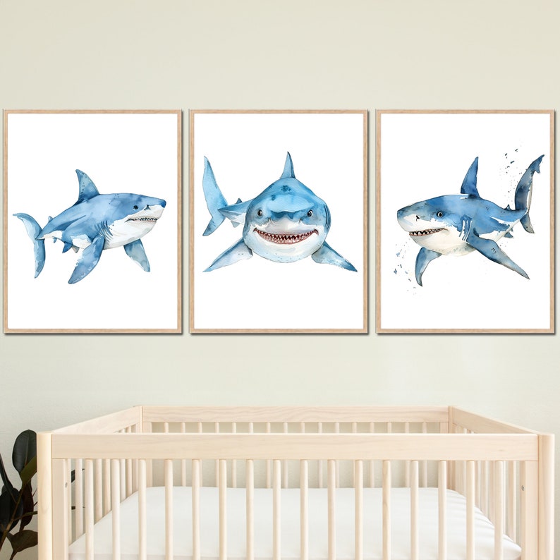 May include: Three framed watercolor paintings of blue sharks on a white background. The sharks are in different poses, with one facing the viewer, one swimming to the right, and one swimming to the left.