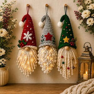 May include: Three hanging gnome ornaments with crocheted hats in red, gray, and green. The red hat features a white snowflake and holly, the gray hat has a red star, and the green hat has a yellow star and small ornaments. Each has a light-up beard.