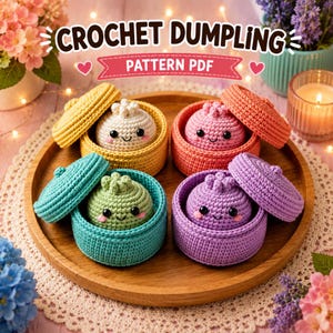 Könnte beinhalten: Vier gehäkelte Knödel mit lächelnden Gesichtern, jeweils in einem passenden Behälter mit Deckel. Die Knödel sind cremefarben, rosa, grün und lila. Der Text CROCHET DUMPLING PATTERN PDF steht über den Objekten auf einem hölzernen Tablett.