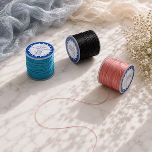 May include: Three cylindrical spools of waxed thread in bright turquoise, solid black, and soft pink. Each spool features a white circular label with blue borders and the text ZEYENS LEATHER CRAFT. The pink thread extends from the spool.