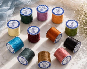Może przedstawiać: Dwanaście szpulek woskowanej nici Zeyen's Leather Craft w różnych kolorach, w tym ciemnozielonym, fioletowym, pomarańczowym, żółtym, bordowym, brązowym, niebieskim, czarnym, oliwkowym i różowym. Każda szpulka ma białą etykietę z niebieskim tekstem i ikoną korony.