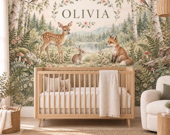 May include: A wooden crib with a white mattress and a white blanket, positioned against a wall mural featuring a forest scene with a deer, a rabbit, a fox, birch trees, and the name OLIVIA printed in the center within a floral wreath design.