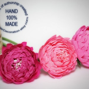 May include: Three paper flowers, one pink and two magenta, arranged in a row on a white surface. The flowers are handmade and have a delicate, layered appearance.