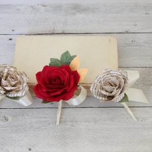 Puede incluir: Tres rosas de papel, una roja y dos de color crema, con detalles de cinta blanca. Las rosas est&aacute;n hechas de p&aacute;ginas de libros.