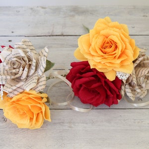 Puede incluir: Un ramo de rosas de papel en tonos rojos, amarillos y crema. Las rosas est&aacute;n hechas de p&aacute;ginas de libros y tela.